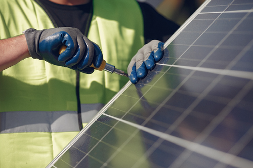 A photo of a solar mechanic wearing a bright green vest, working on a solar panel